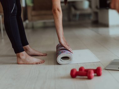 Spor elbiseli genç bir kadın oturma odasında online antrenman için spor malzemeleri hazırlıyor..