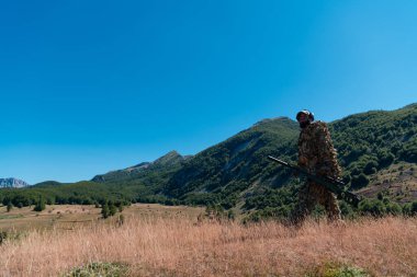Ordu askeri dürbünlü bir keskin nişancı tüfeği tutuyor ve ormanda yürüyor. savaş, ordu, teknoloji ve insanlar kavramı