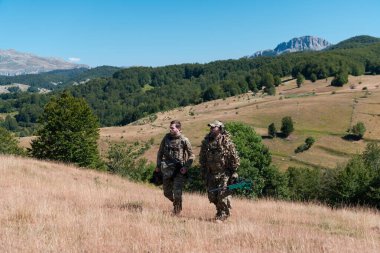 Bir keskin nişancı timi gizli göreve gidiyor. Keskin nişancı asistanı ve takım lideri sarı çimenler ve mavi gökyüzü ile doğaya doğru yürüyor ve nişan alıyor. Taktik kamuflaj üniforması.