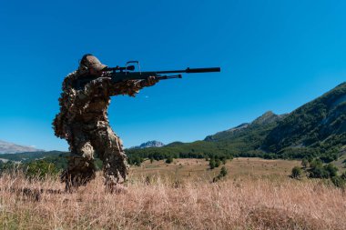 Ordu askeri dürbünlü bir keskin nişancı tüfeği tutuyor ve ormanda yürüyor. savaş, ordu, teknoloji ve insanlar kavramı
