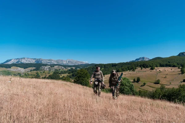 狙撃チームの部隊が潜入してる 黄色い草と青い空で自然を歩き 目指す狙撃手のアシスタントとチームリーダー 実用的な迷彩制服 — ストック写真