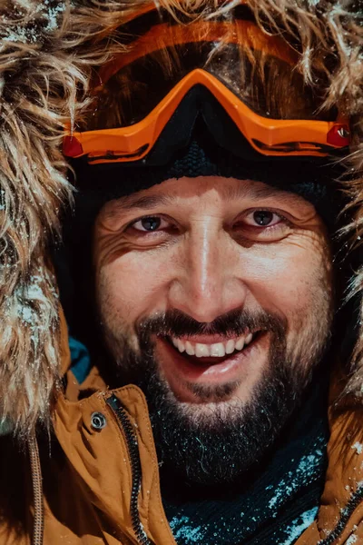 Head shot of a man in a cold snowy area wearing a thick brown winter jacket, snow goggles and gloves on a cold Scandinavian night. Life in the cold regions of the country