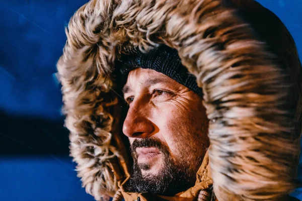 Head shot of a man in a cold snowy area wearing a thick brown winter jacket, snow goggles and gloves on a cold Scandinavian night. Life in the cold regions of the country