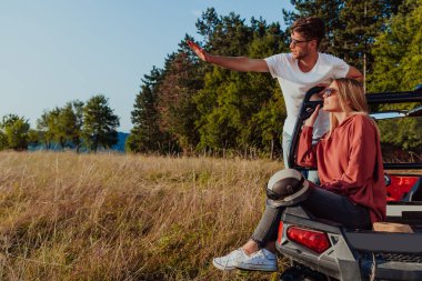 Young happy excited couple enjoying beautiful sunny day while driving a off road buggy car on mountain nature. 