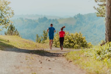 Couple enjoying in a healthy lifestyle while jogging on a country road through the beautiful sunny forest, exercise and fitness concept. 
