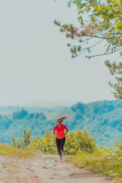 Genç ve mutlu bir kadın sağlıklı bir hayat sürerken güzel güneşli orman, egzersiz ve zindelik konsepti boyunca bir kır yolunda koşuyor.. 
