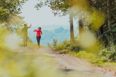 Couple enjoying in a healthy lifestyle while jogging on a country road through the beautiful sunny forest, exercise and fitness concept. 
