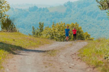 Couple enjoying in a healthy lifestyle while jogging on a country road through the beautiful sunny forest, exercise and fitness concept. 