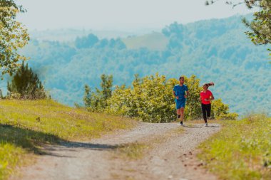 Couple enjoying in a healthy lifestyle while jogging on a country road through the beautiful sunny forest, exercise and fitness concept. 