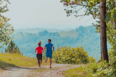 Couple enjoying in a healthy lifestyle while jogging on a country road through the beautiful sunny forest, exercise and fitness concept. 
