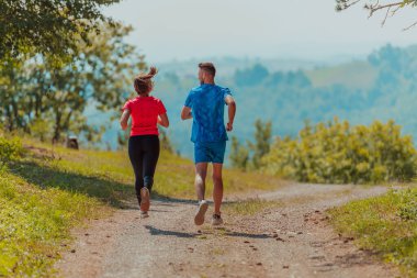 Couple enjoying in a healthy lifestyle while jogging on a country road through the beautiful sunny forest, exercise and fitness concept. 