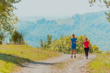 Couple enjoying in a healthy lifestyle while jogging on a country road through the beautiful sunny forest, exercise and fitness concept. 