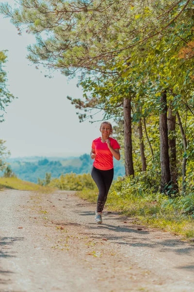 Genç ve mutlu bir kadın sağlıklı bir hayat sürerken güzel güneşli orman, egzersiz ve zindelik konsepti boyunca bir kır yolunda koşuyor.. 