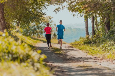 Couple enjoying in a healthy lifestyle while jogging on a country road through the beautiful sunny forest, exercise and fitness concept. 