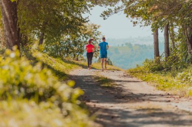 Couple enjoying in a healthy lifestyle while jogging on a country road through the beautiful sunny forest, exercise and fitness concept. 