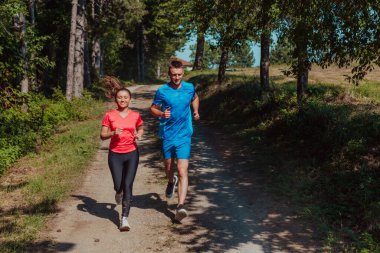 Couple enjoying in a healthy lifestyle while jogging on a country road through the beautiful sunny forest, exercise and fitness concept. 