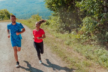 Couple enjoying in a healthy lifestyle while jogging on a country road through the beautiful sunny forest, exercise and fitness concept. 