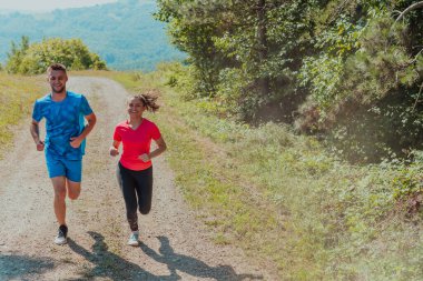 Couple enjoying in a healthy lifestyle while jogging on a country road through the beautiful sunny forest, exercise and fitness concept. 