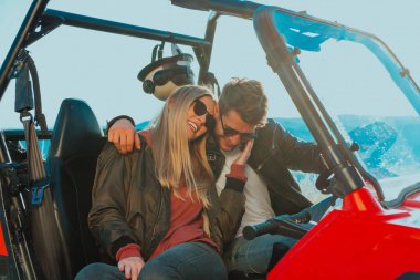 Young happy excited couple enjoying beautiful sunny day while driving a off road buggy car on mountain nature. 
