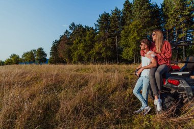 Young happy excited couple enjoying beautiful sunny day while driving a off road buggy car on mountain nature. 