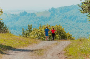 Couple enjoying in a healthy lifestyle while jogging on a country road through the beautiful sunny forest, exercise and fitness concept. 