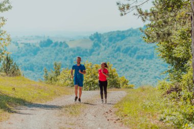 Couple enjoying in a healthy lifestyle while jogging on a country road through the beautiful sunny forest, exercise and fitness concept. 