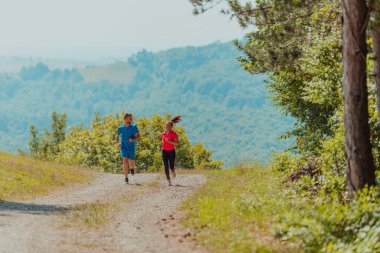 Couple enjoying in a healthy lifestyle while jogging on a country road through the beautiful sunny forest, exercise and fitness concept. 
