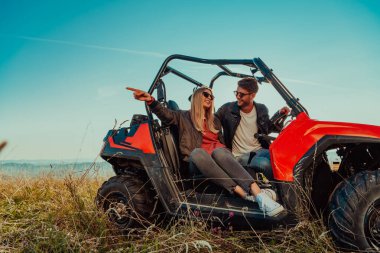 Young happy excited couple enjoying beautiful sunny day while driving a off road buggy car on mountain nature. 