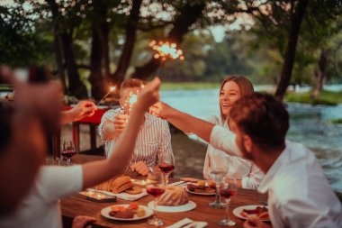 Bir grup mutlu arkadaş tatil tatillerini fıskiyelerle kutlarken ve kırmızı şarap içerken aynı zamanda güzel bir yaz akşamı nehir kenarında piknik yapıyorlar.. 
