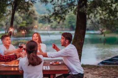 Bir grup mutlu arkadaş tatil tatillerini fıskiyelerle kutlarken ve kırmızı şarap içerken aynı zamanda güzel bir yaz akşamı nehir kenarında piknik yapıyorlar.. 