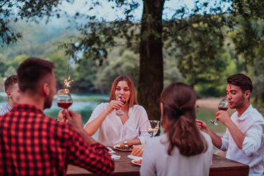 Bir grup mutlu arkadaş tatil tatillerini fıskiyelerle kutlarken ve kırmızı şarap içerken aynı zamanda güzel bir yaz akşamı nehir kenarında piknik yapıyorlar.. 