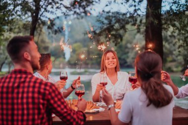 Bir grup mutlu arkadaş tatil tatillerini fıskiyelerle kutlarken ve kırmızı şarap içerken aynı zamanda güzel bir yaz akşamı nehir kenarında piknik yapıyorlar.. 