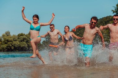 A group of diverse young people having fun together as they run along the river and play water games. 