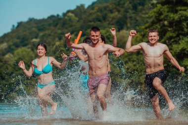A group of diverse young people having fun together as they run along the river and play water games. 