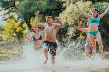 A group of diverse young people having fun together as they run along the river and play water games. 