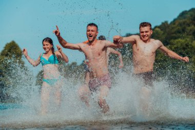 A group of diverse young people having fun together as they run along the river and play water games. 