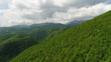 Aerial drone overhead of single car driving down curvy mountain road through green forest valley with trees and rainy fog. High quality 4k footage