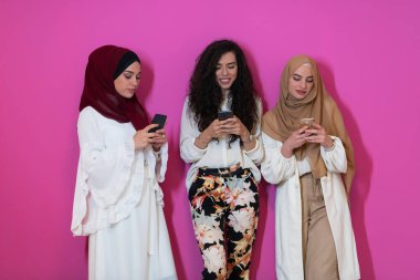 İkisi tesettürlü, şık giyinen, pembe arka planda izole cep telefonu kullanan, modern İslami moda teknolojisi ve ramazan kareem kavramını temsil eden bir grup güzel Müslüman kadın.. 