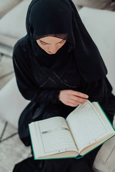 Νεαρή Παραδοσιακή Μουσουλμάνα Γυναίκα Που Διαβάζει Κοράνι Στον Καναπέ Πριν — Φωτογραφία Αρχείου