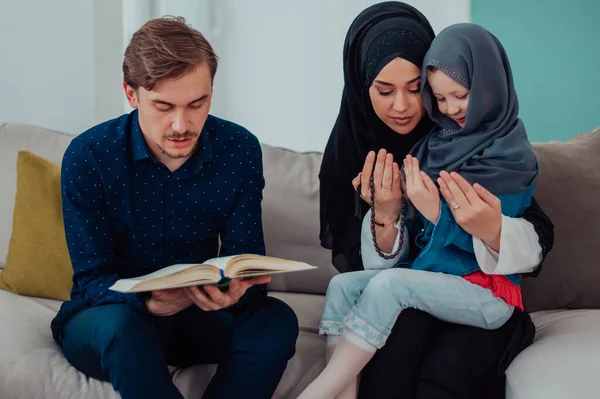 Happy Muslim family enjoying the holy month of Ramadan while praying and reading the Quran together in a modern home.