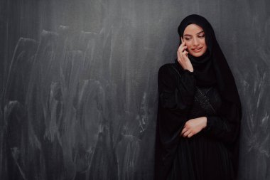 Genç, modern Müslüman iş kadını siyah karatahtanın önünde tesettürlü kıyafetler giyiyor.. 