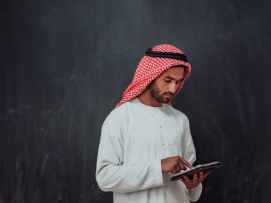 Genç Arap Müslüman iş adamı siyah karatahtanın önünde tesettürlü kıyafetler giyerek tablet bilgisayar kullanıyor. 
