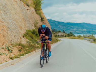 Full length portrait of an active triathlete in sportswear and with a protective helmet riding a bicycle. Selective focus . 