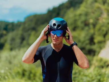 Close up photo of an active triathlete in sportswear and with a protective helmet riding a bicycle. Selective focus. 