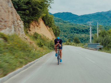 Full length portrait of an active triathlete in sportswear and with a protective helmet riding a bicycle. Selective focus . 
