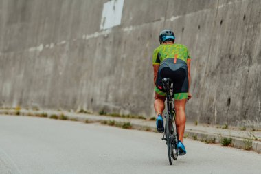 Full length portrait of an active triathlete in sportswear and with a protective helmet riding a bicycle. Selective focus . 