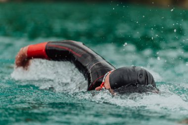 A triathlete in a professional swimming suit trains on the river while preparing for Olympic swimming. 