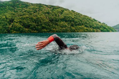 A triathlete in a professional swimming suit trains on the river while preparing for Olympic swimming. 