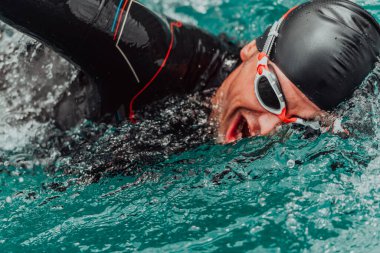 A triathlete in a professional swimming suit trains on the river while preparing for Olympic swimming. 