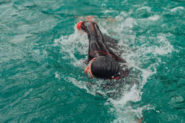 A triathlete in a professional swimming suit trains on the river while preparing for Olympic swimming. 
